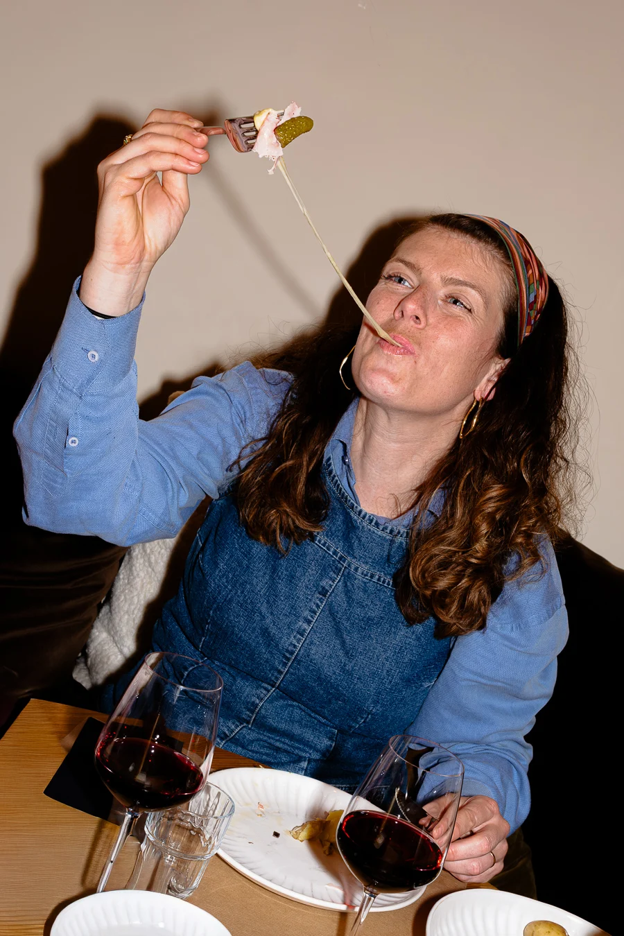 femme mange de la raclette un filet de fromage pend entre sa bouche et la fourchette