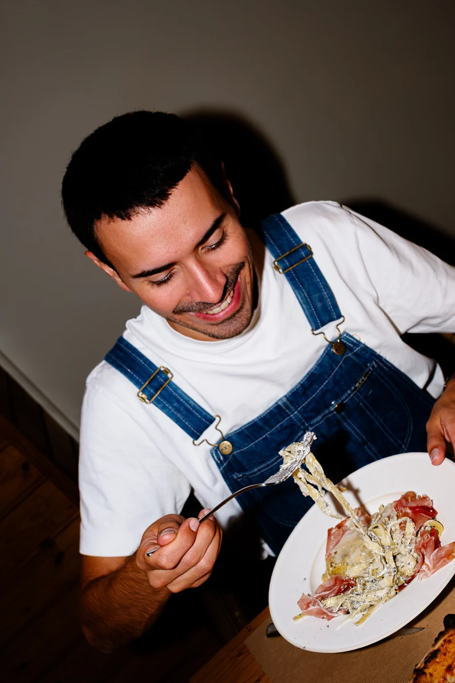 homme en salopette bleue et t-shirt blanc mange des pâtes fraîches aux truffes et rigole shooting culinaire Chalet des dunes