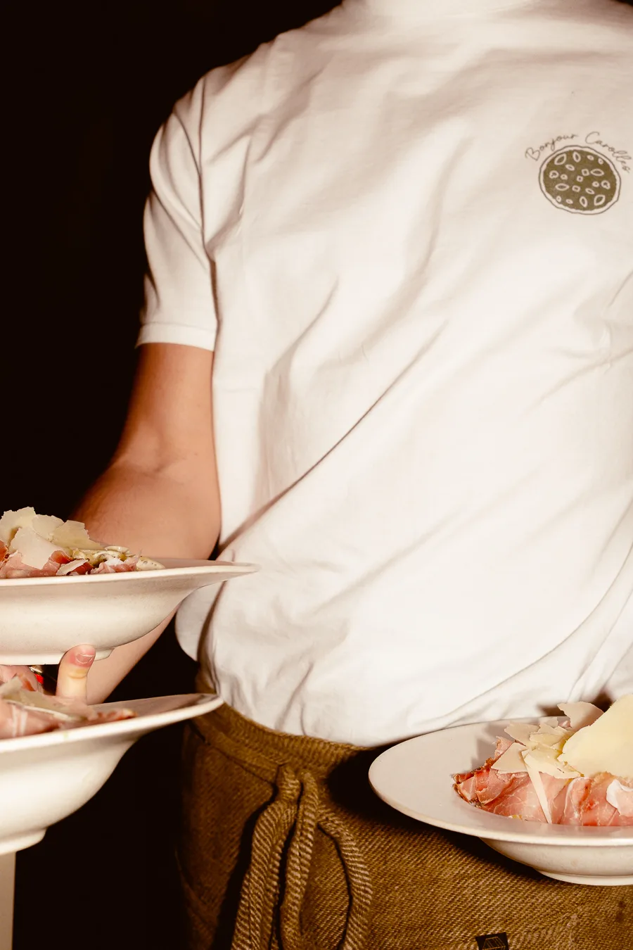 un serveur tient trois assiettes rondes avec des pâtes dedans et du jambon italien