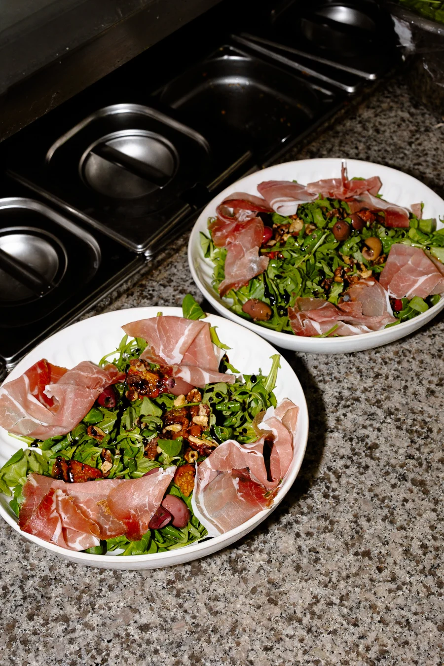 deux assiettes de salade avec du jambon cru dans une cuisine