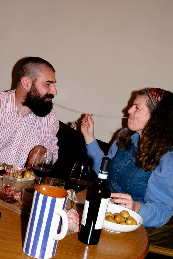 couple homme et femme lange de la raclette avec un filet de fromage entre leur bouche shooting culinaire