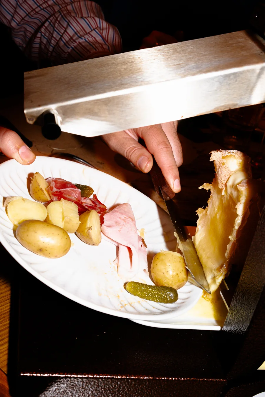 une assiette avec du jambon blanc, des pommes de terre, un cornichon et du fromage à raclette qui fond shooting culinaire