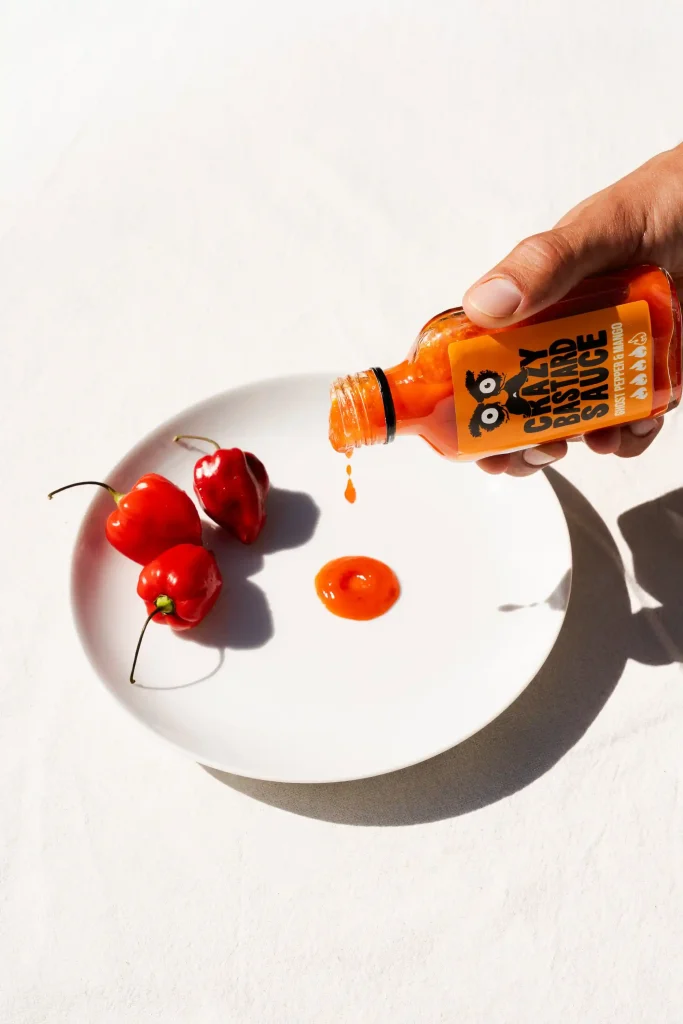 main versant une goutte de sauce piquante sur assiette blanche crazy bastard sauce photographie culinaire ciao tutti studio nantes